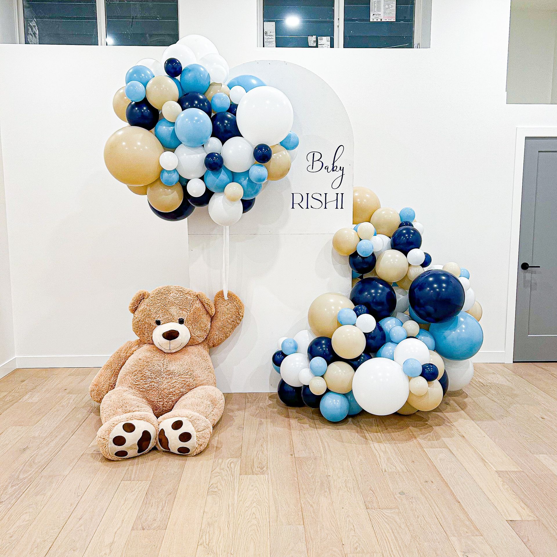 A teddy bear is sitting in front of a wall covered in balloons.