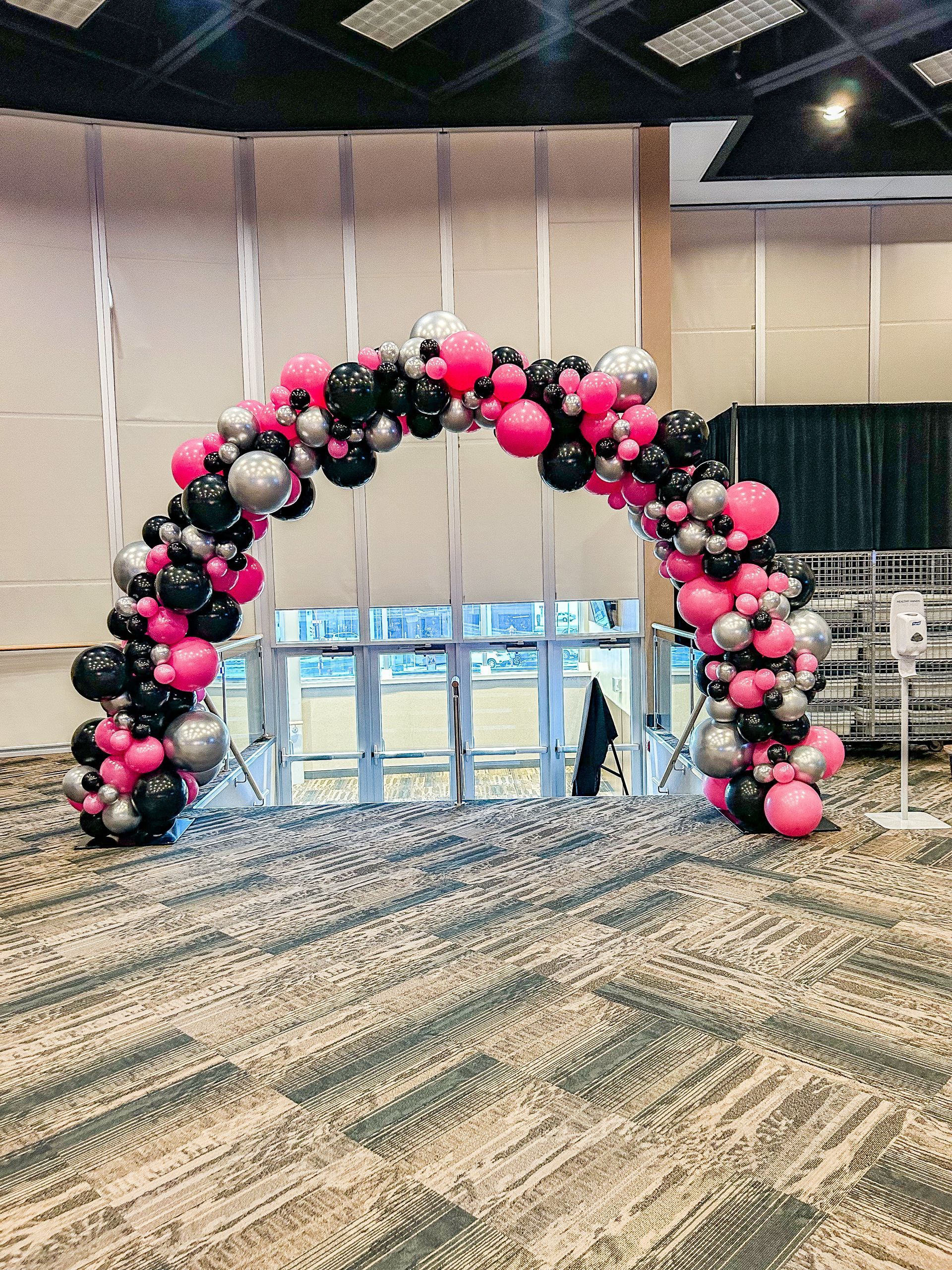 A large arch made of pink , black and silver balloons in a room.