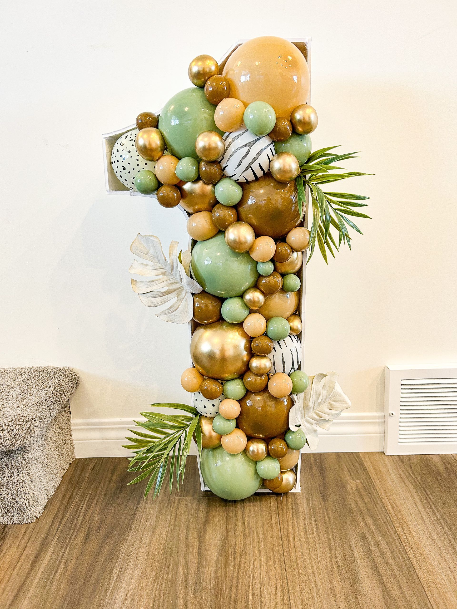 A large number one made of balloons is sitting on a wooden floor.