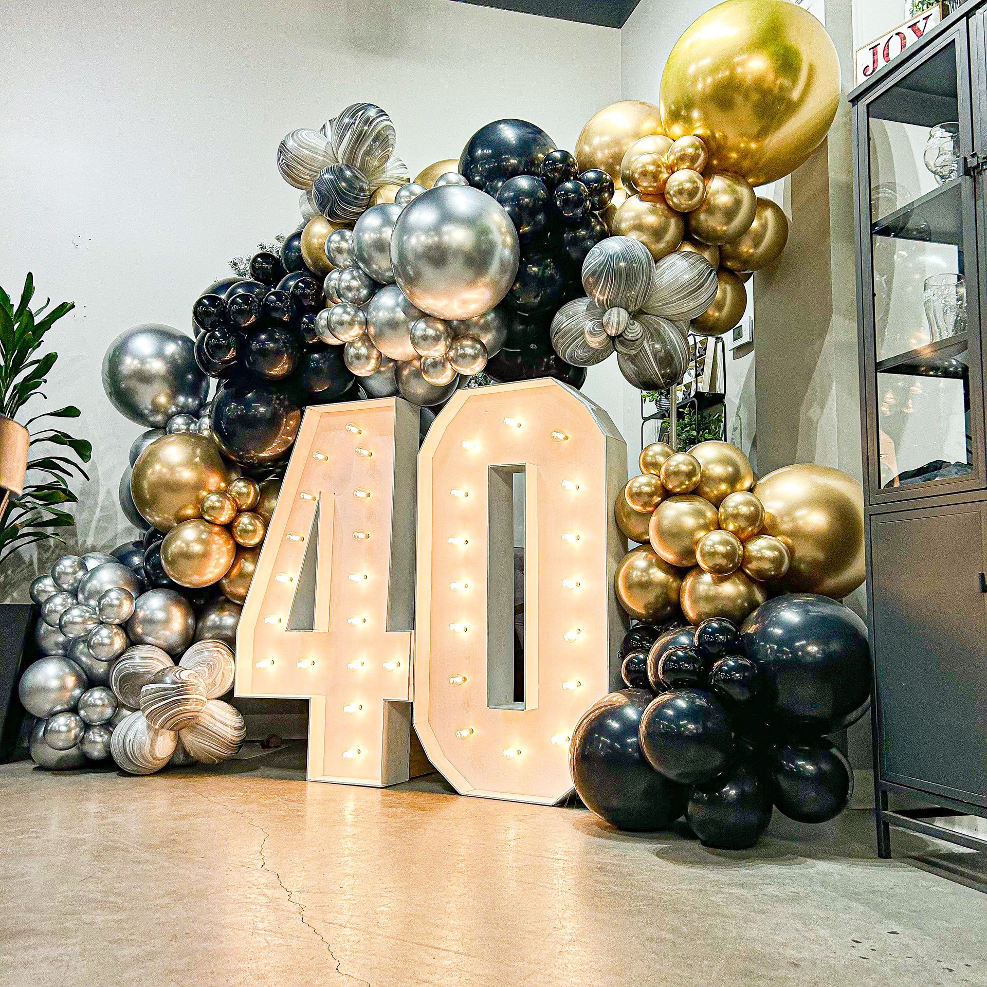 A large number 40 is surrounded by balloons in a room.