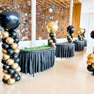 A row of tables decorated with black and gold balloons.