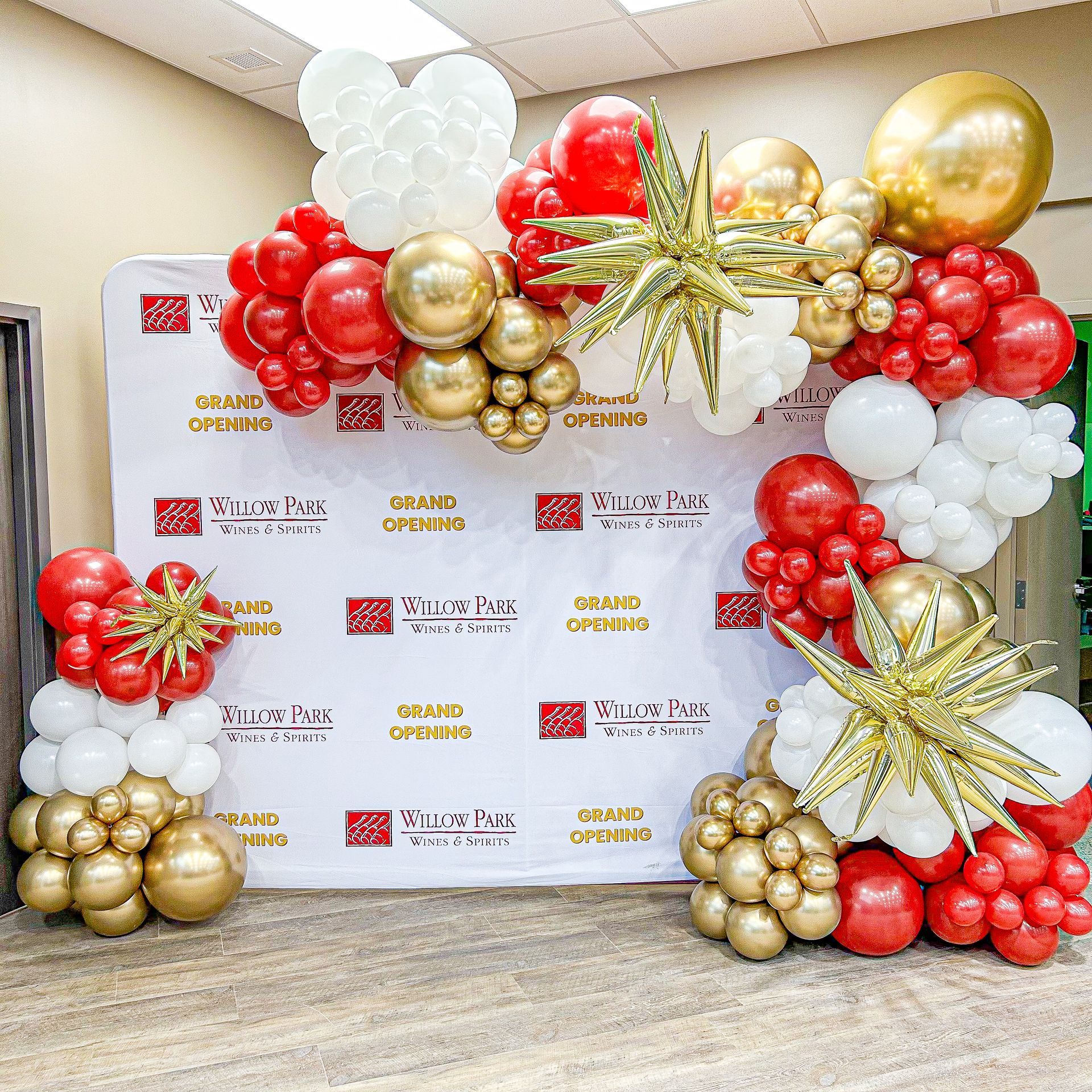 A wall is decorated with red , white and gold balloons.