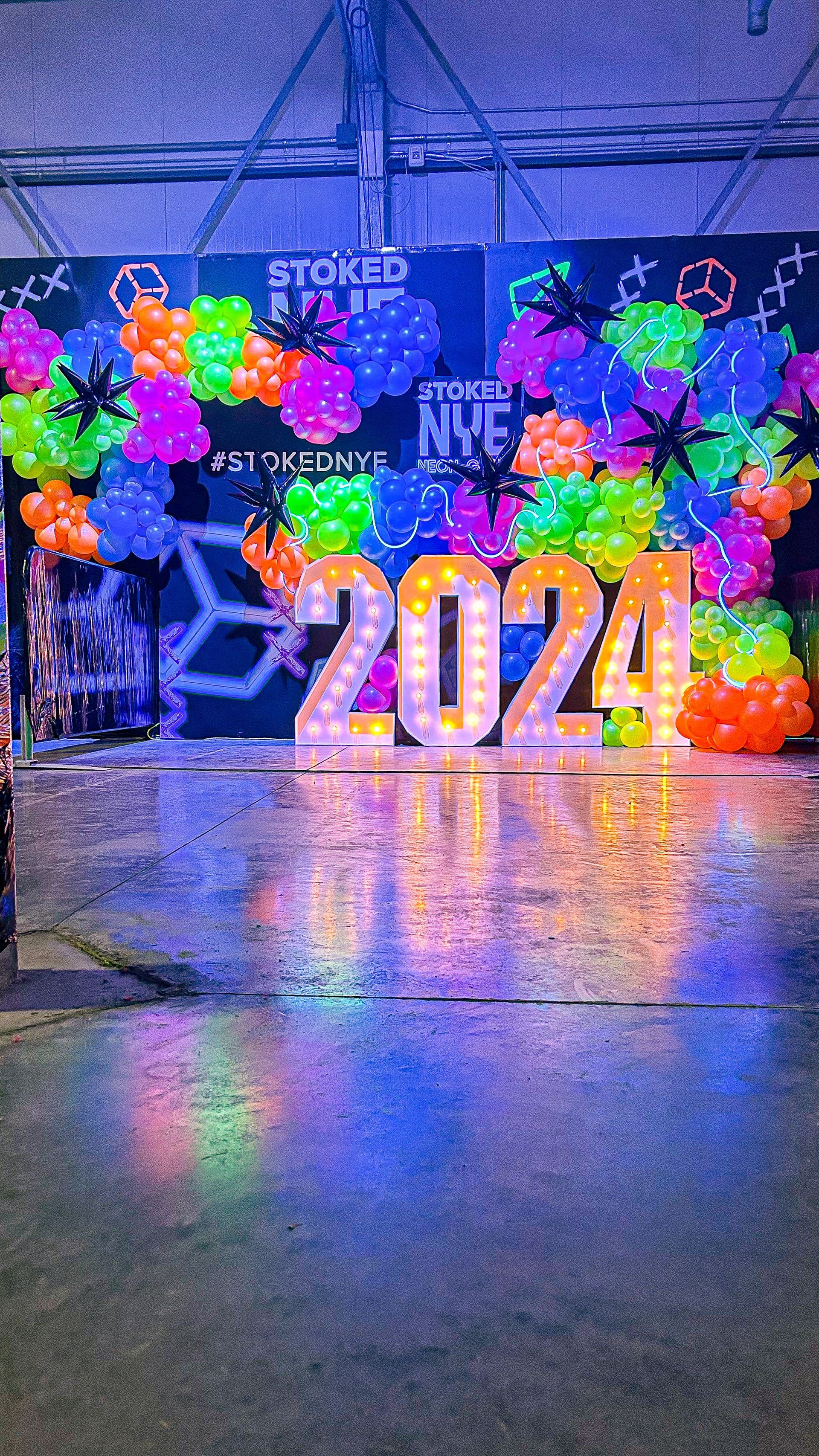 A stage is decorated with neon balloons and lights for a new year 's eve party.