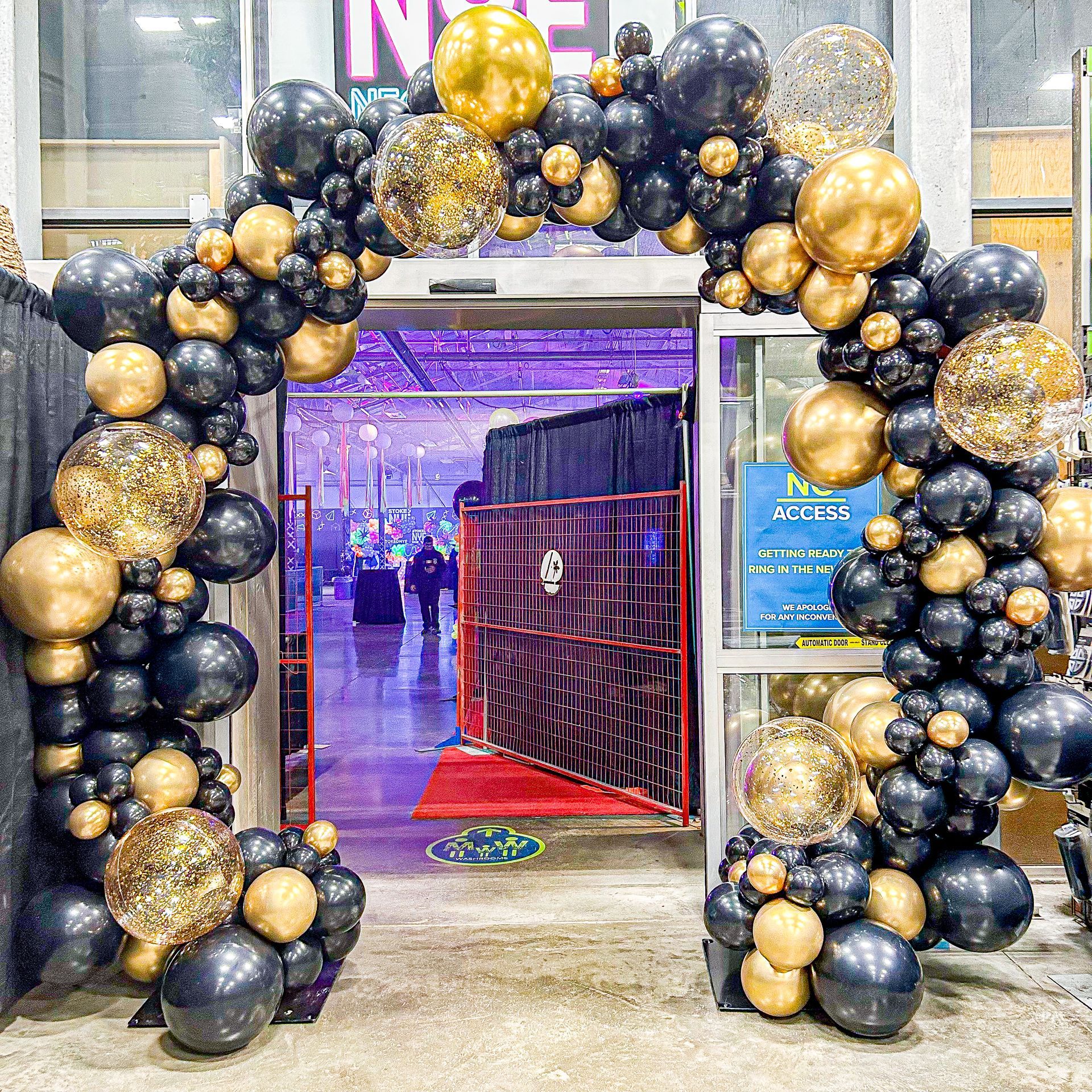 A large arch made of black and gold balloons is in front of a building.