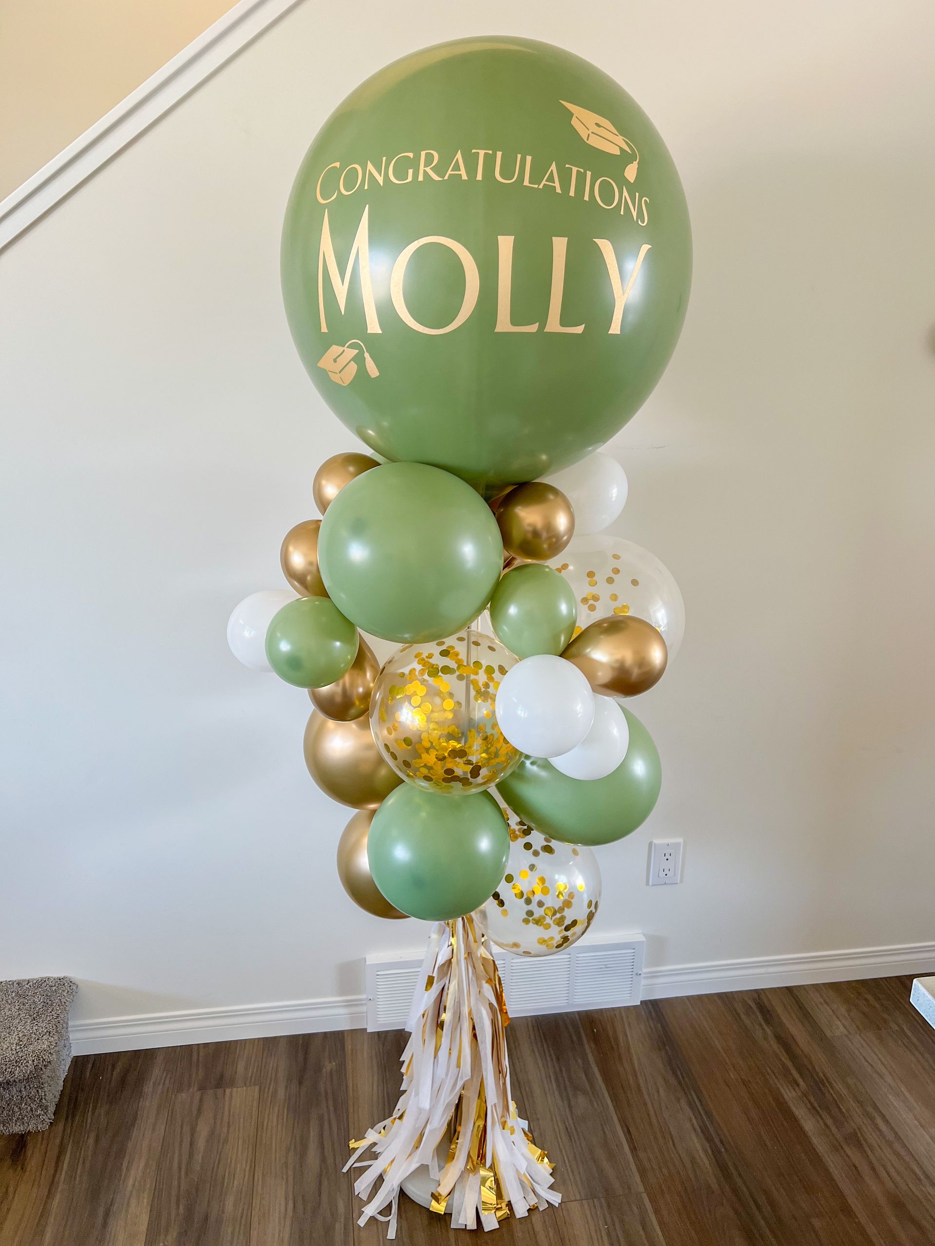 A bunch of green and gold balloons are sitting on a wooden floor.