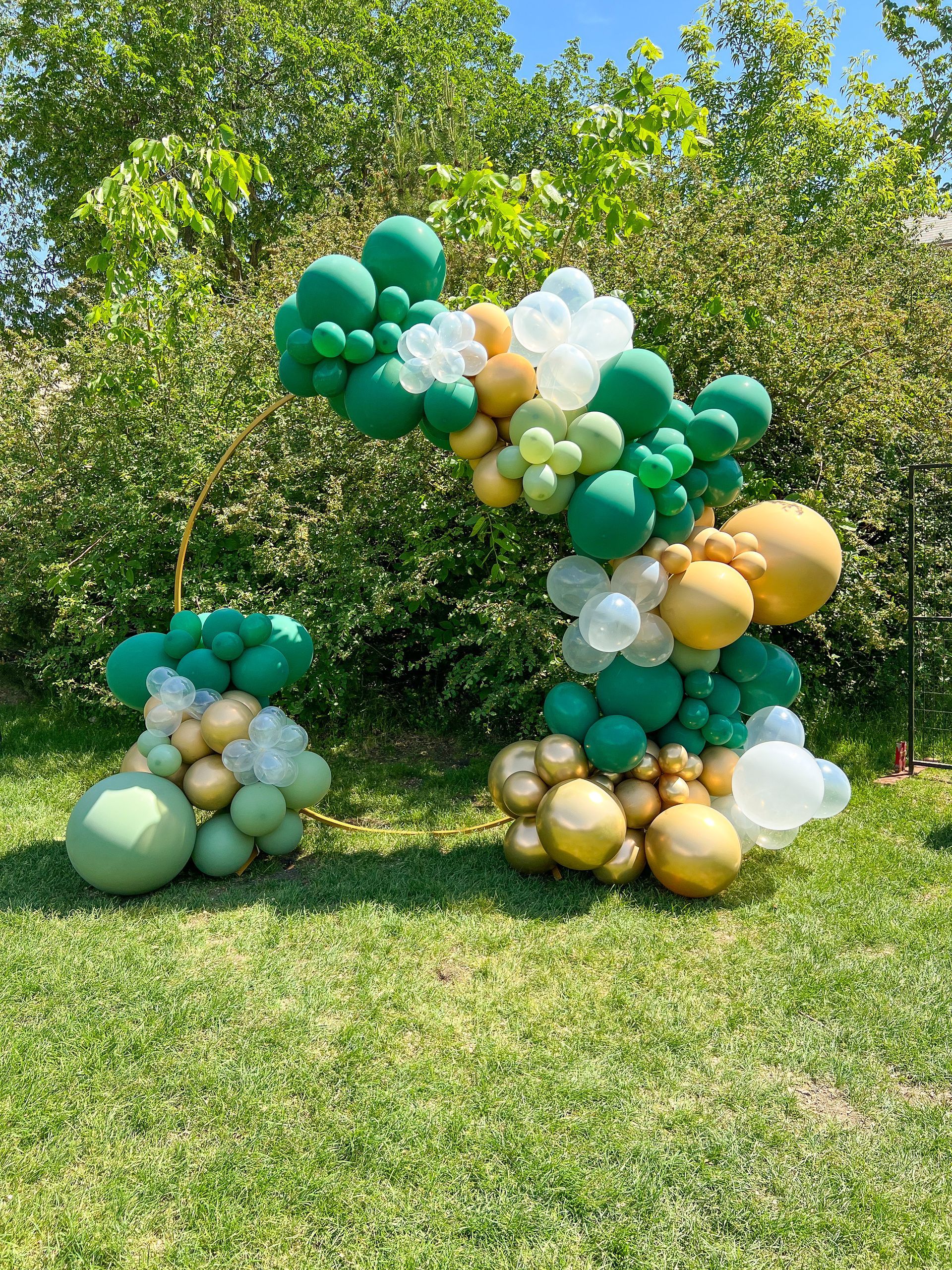 A bunch of green and gold balloons are sitting on top of a lush green field.