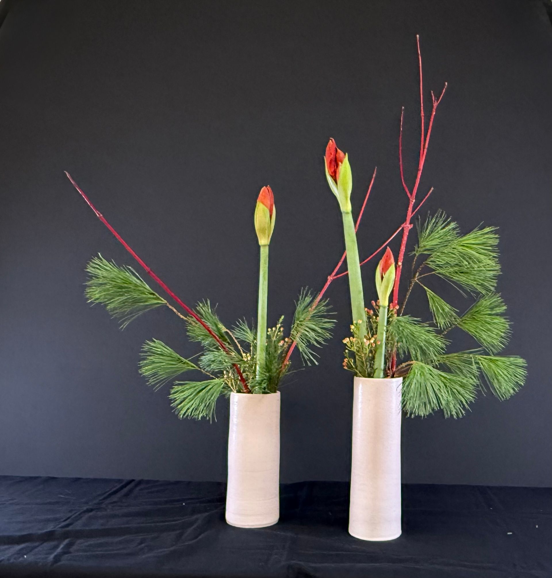 Twee bloemstukken in cilindervormige vazen ​​met rode stelen, groen blad en rode bloemknoppen.