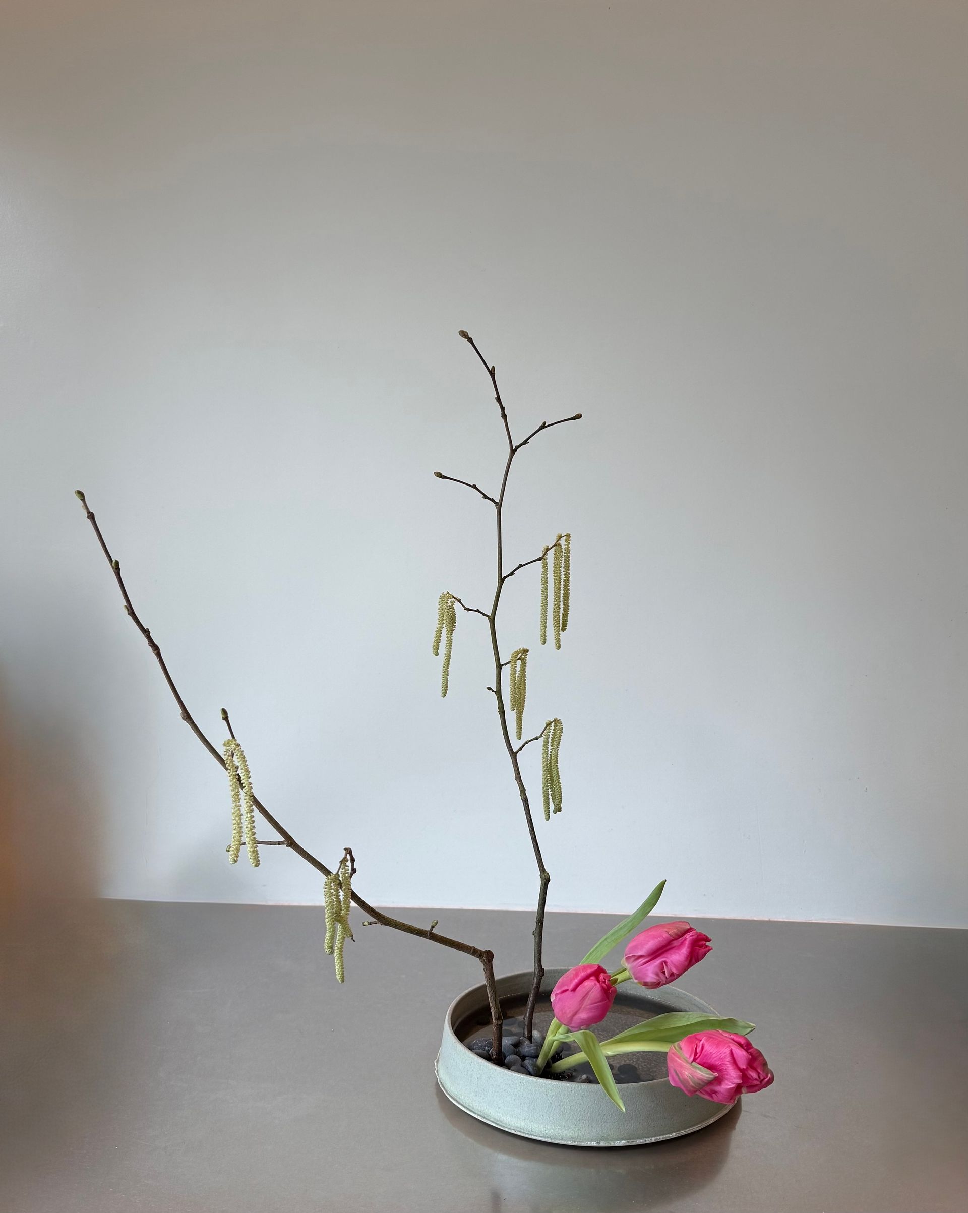 Ikebana bloemstuk met drie roze tulpen en takken met katjes in een blauwe vaas.