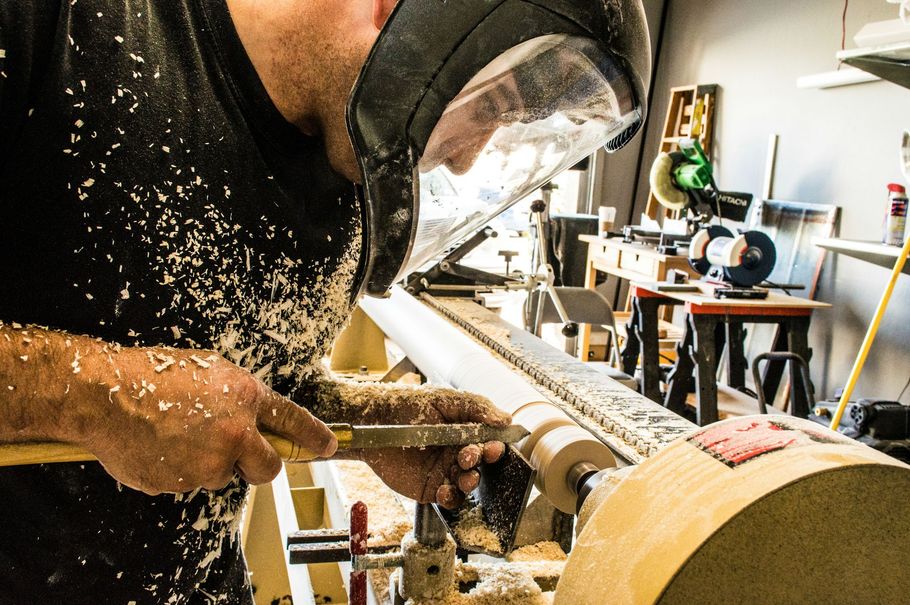 Person using a lathe to shape wood, with wood shavings flying in a workshop.