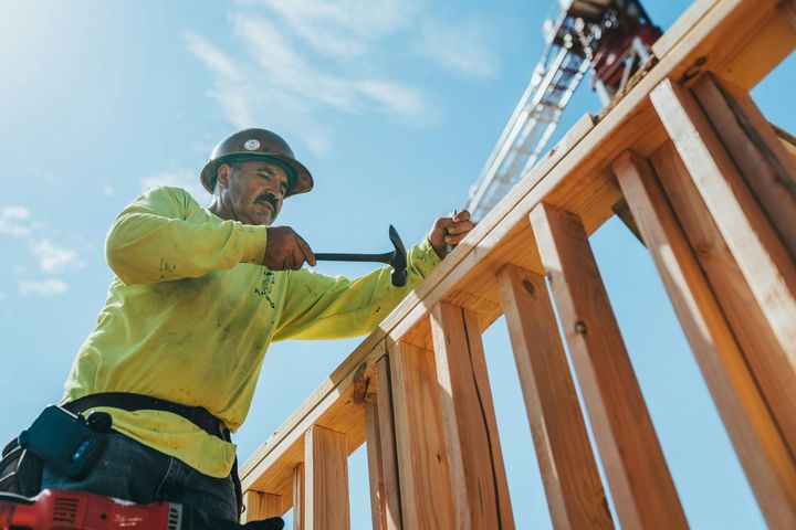 Construction worker hammering wooden framing under a clear blue sky