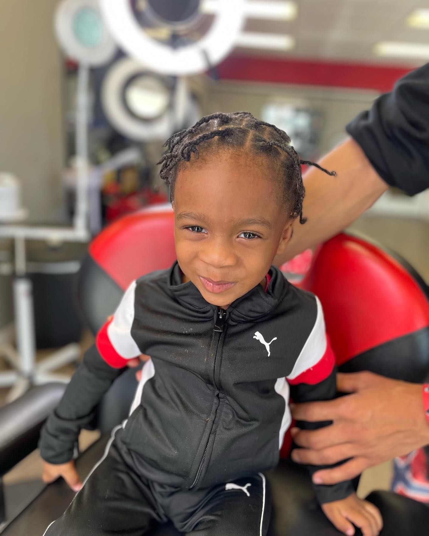 A little boy is sitting in a chair wearing a puma jacket.