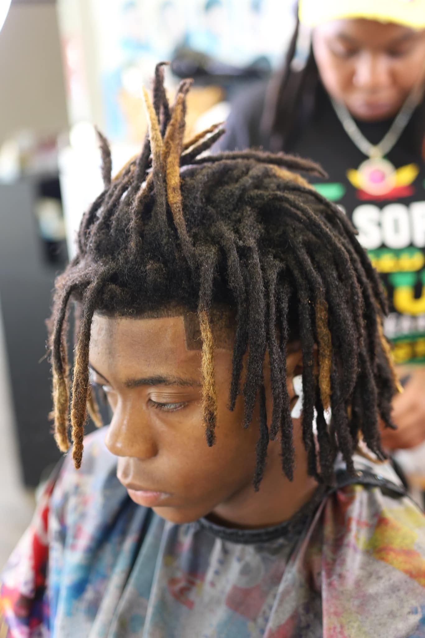 A man with dreadlocks is getting his hair cut in a salon.