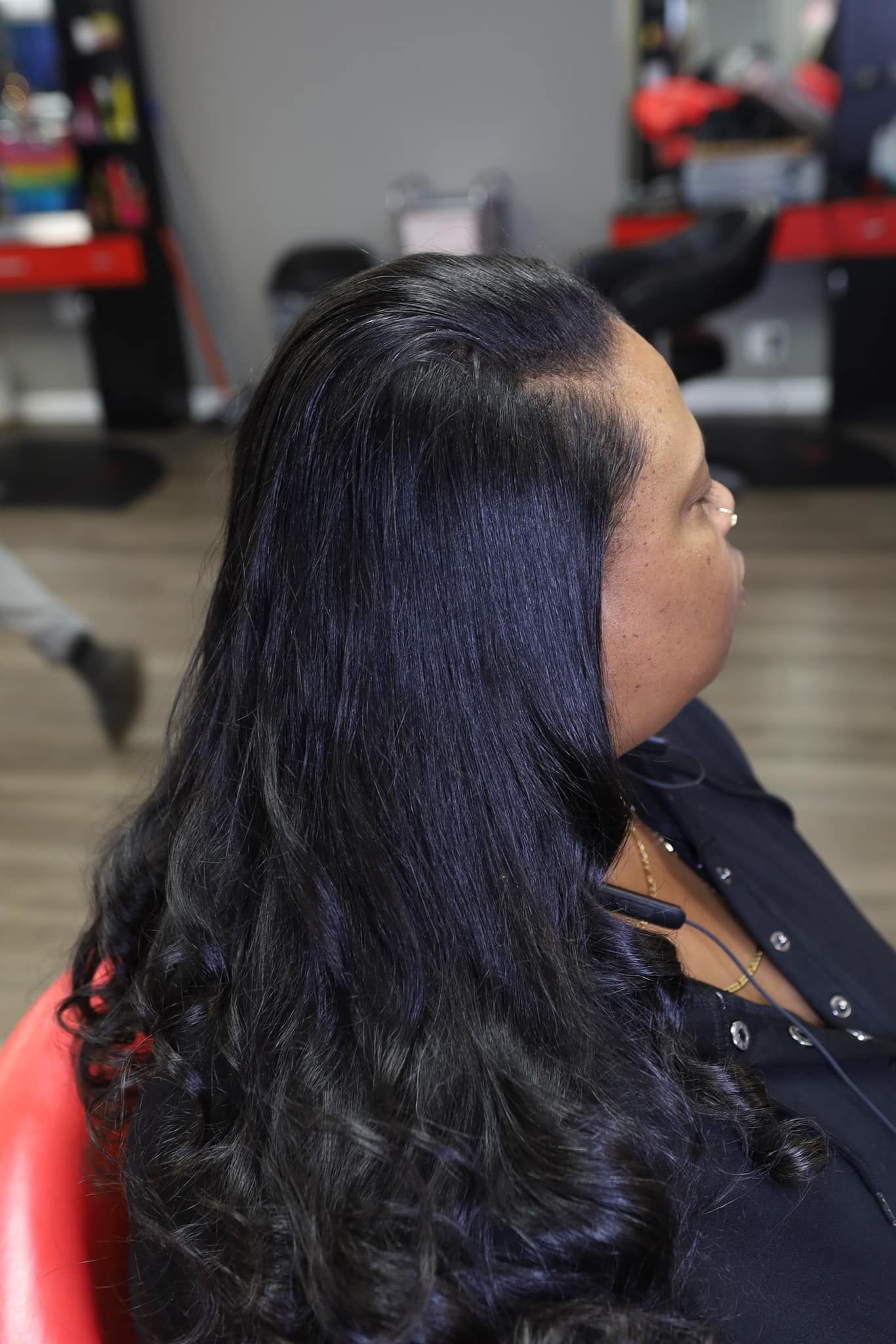 A woman with long black hair is sitting in a red chair in a salon.
