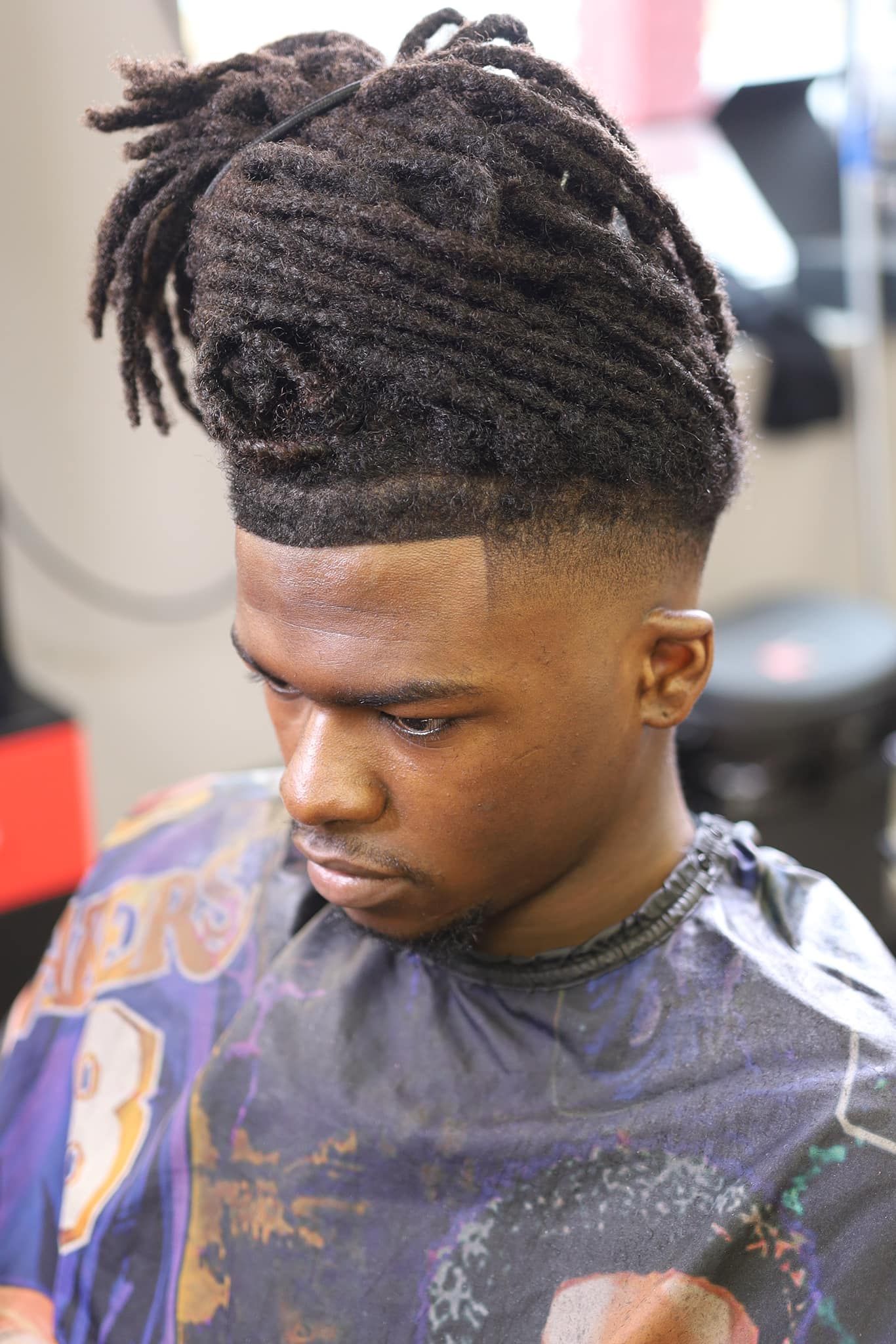A man with dreadlocks is getting his hair cut at a barber shop.