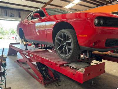 A bright red Dodge Challenger sits raised on a red automotive scissor lift inside a repair shop. | Rapid Auto and Truck Repair
