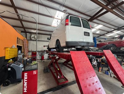 A white van is raised on a red automotive lift in a workshop, with a Hunter wheel alignment system visible in the foreground. | Rapid Auto and Truck Repair