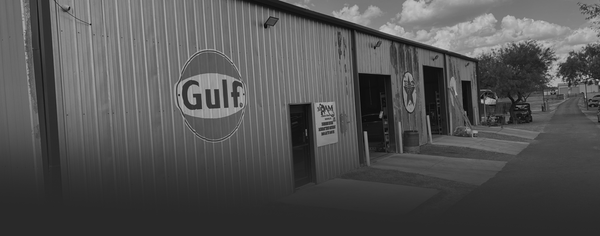 A black and white image of a metal industrial building with a Gulf Oil logo on the wall and several open service bays. | Rapid Auto and Truck Repair
