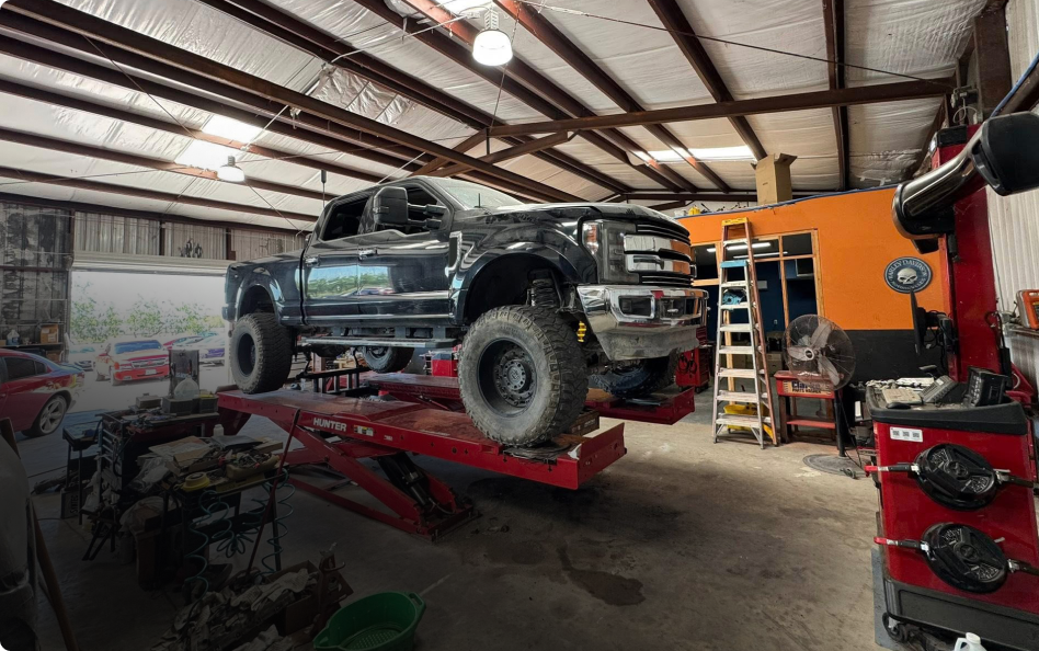 A lifted black pickup truck sits on a red hydraulic lift inside an automotive repair shop with tools and equipment. | Rapid Auto and Truck Repair