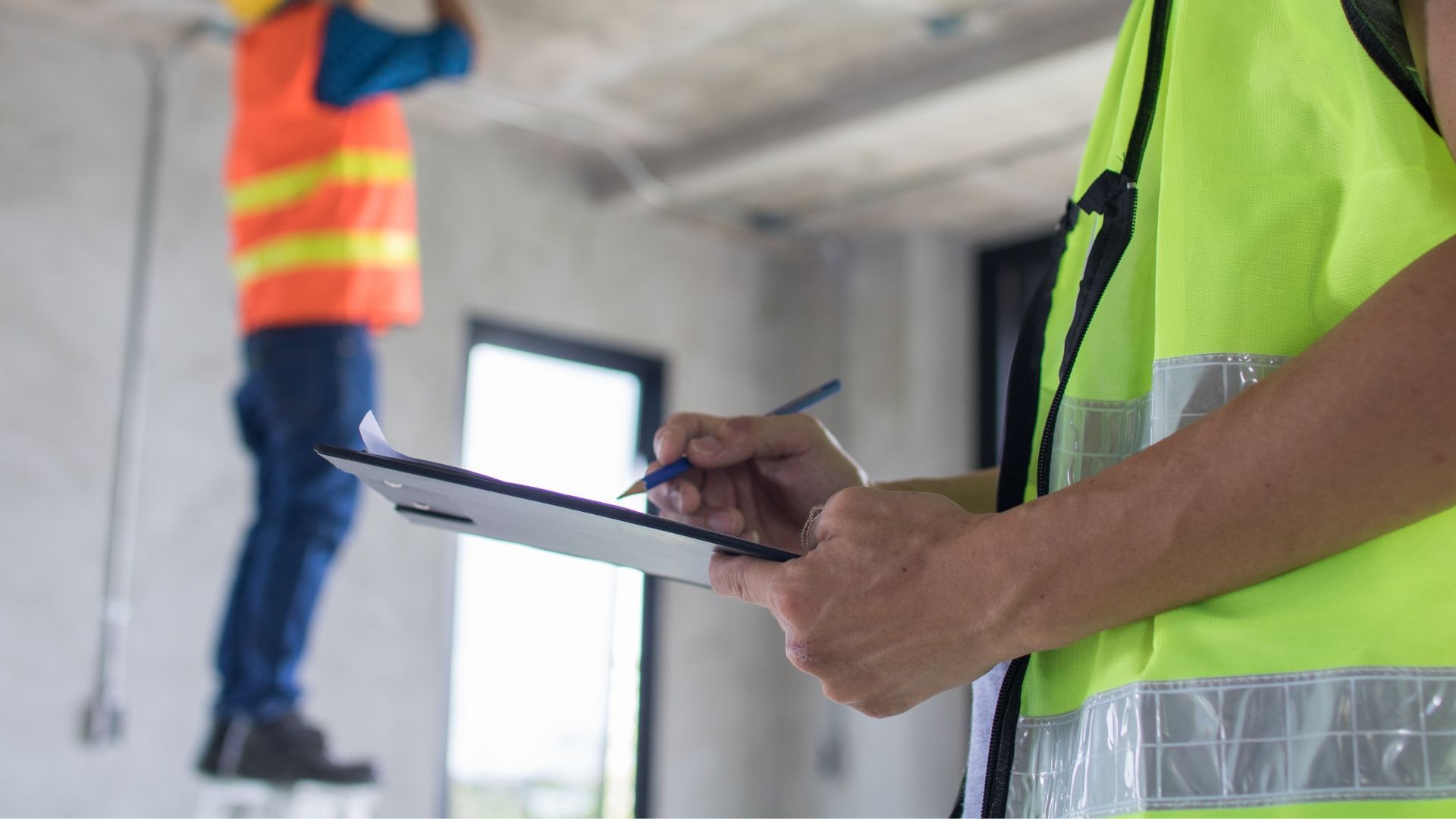 Construction worker in safety vest taking notes while another works.