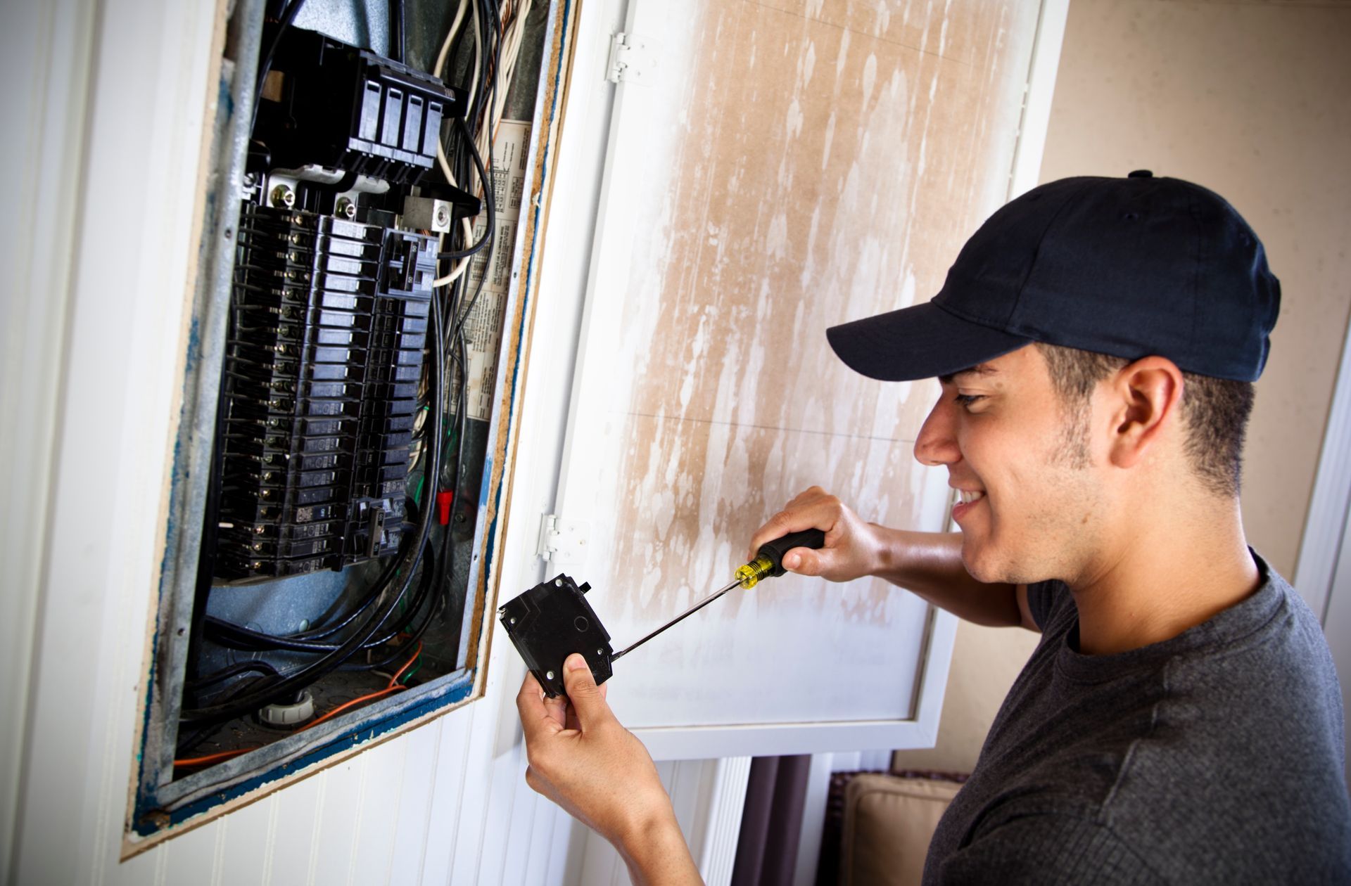 A man is working on an electrical box with a screwdriver.