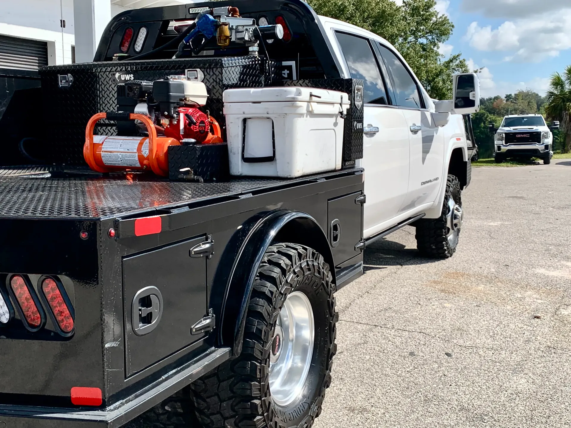 White pickup truck with a black flatbed utility body equipped with a red air compressor and a white cooler | Infinity Tires and Auto Repair