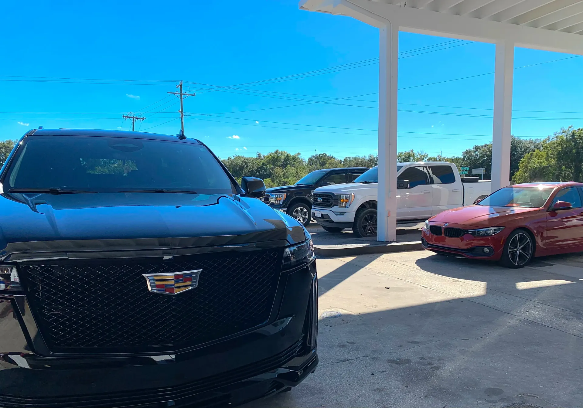 A black Cadillac SUV in the foreground with a white pickup truck and a red sedan parked | Infinity Tires and Auto Repair