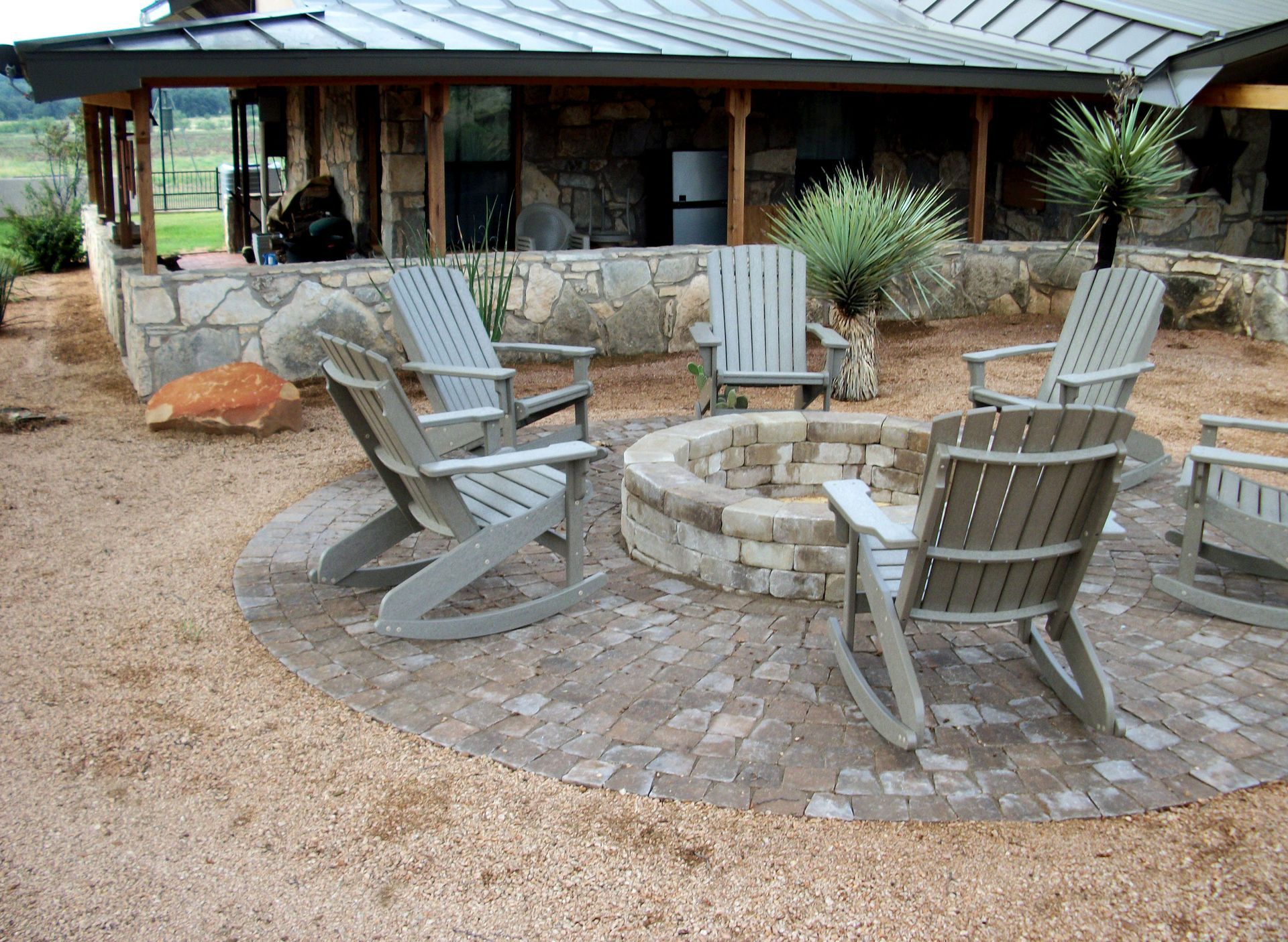 Rocking chairs around a fire pit in front of a house