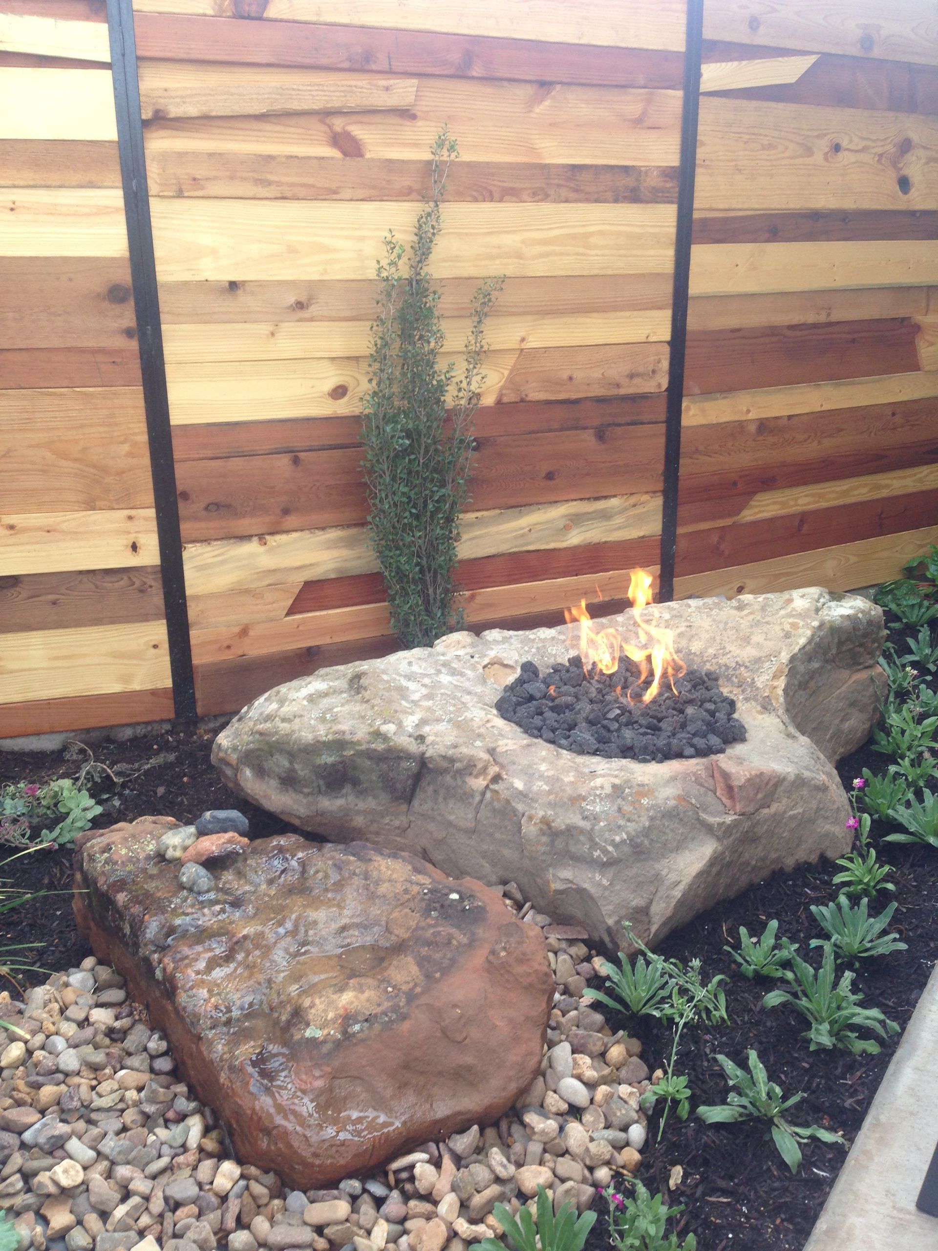 A fire pit is surrounded by rocks and a wooden fence