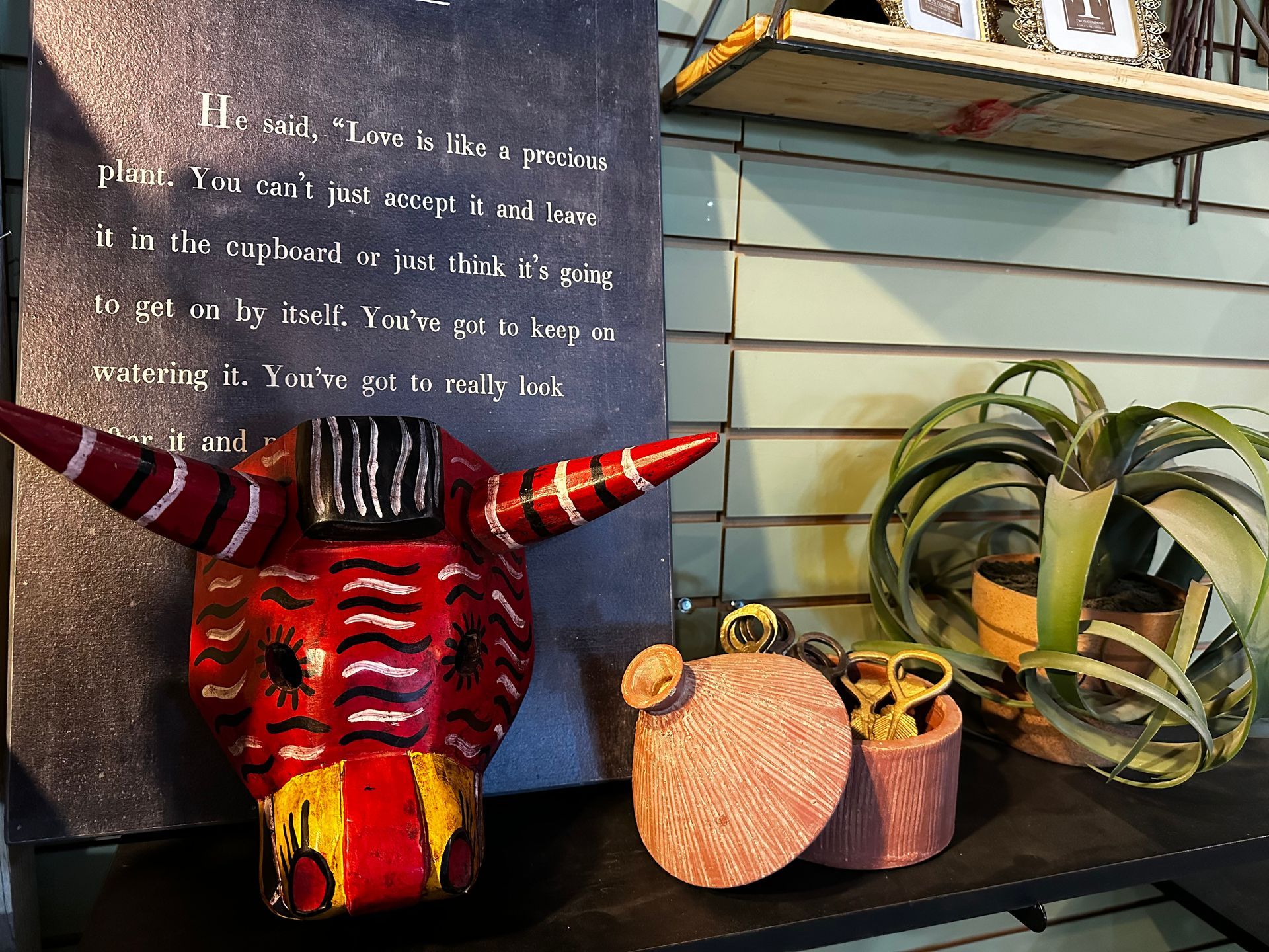 A red mask with horns is on a shelf next to a plant