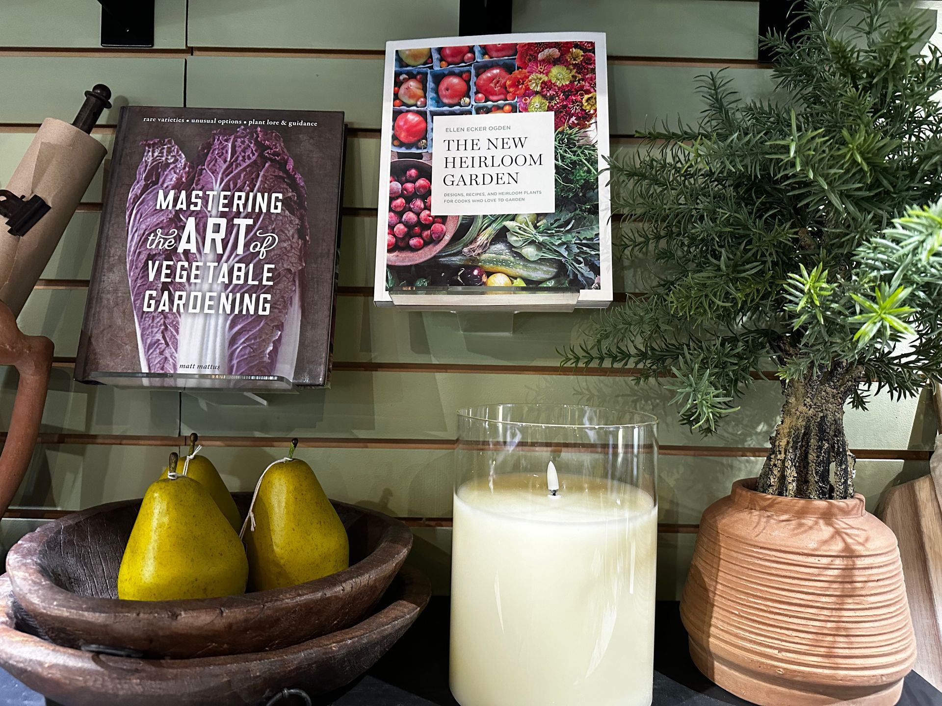 A candle is sitting on a table next to a bowl of pears and a book on vegetable gardening.