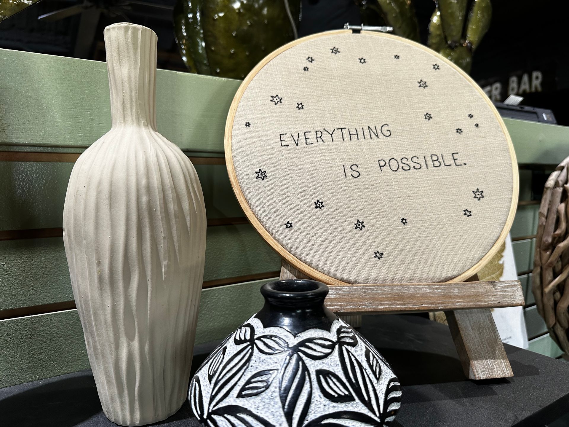 A embroidery hoop with the words `` everything is possible '' is sitting on a table next to a vase.
