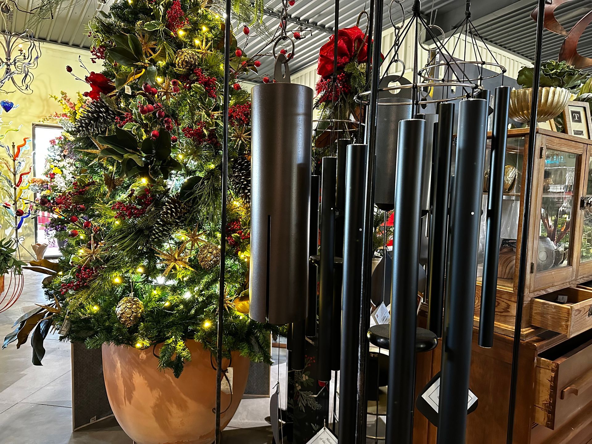 A christmas tree is in a pot next to a row of wind chimes.