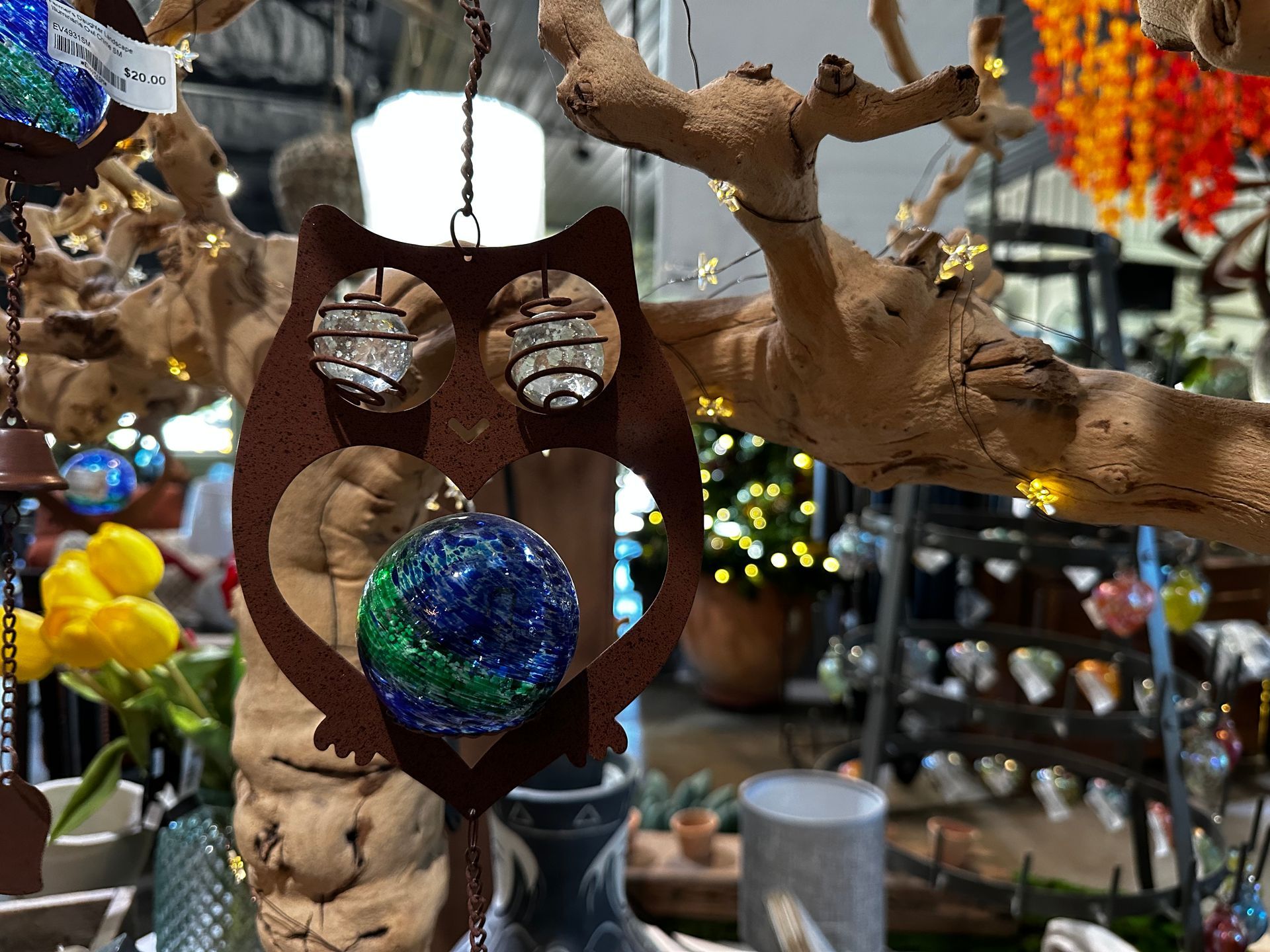 An owl wind chime is hanging from a tree branch in a store.