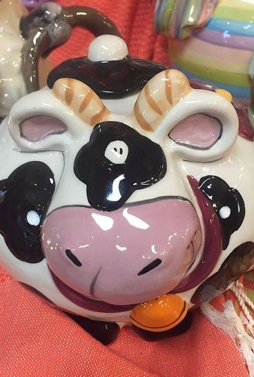 A ceramic cow shaped teapot is sitting on a pink cloth.