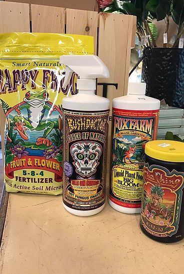 Three bottles of fertilizer are sitting on a wooden table next to a bag of fertilizer.