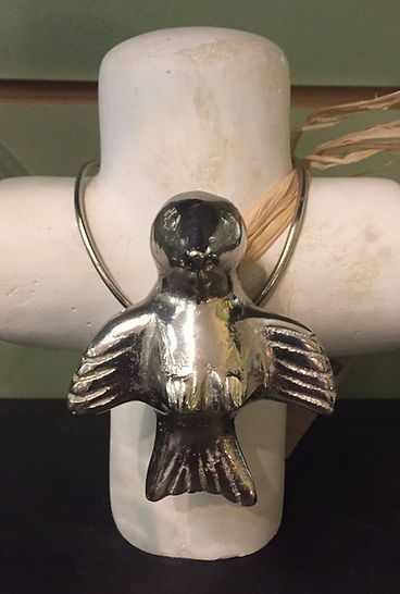 A silver bird necklace is sitting on top of a white cross.