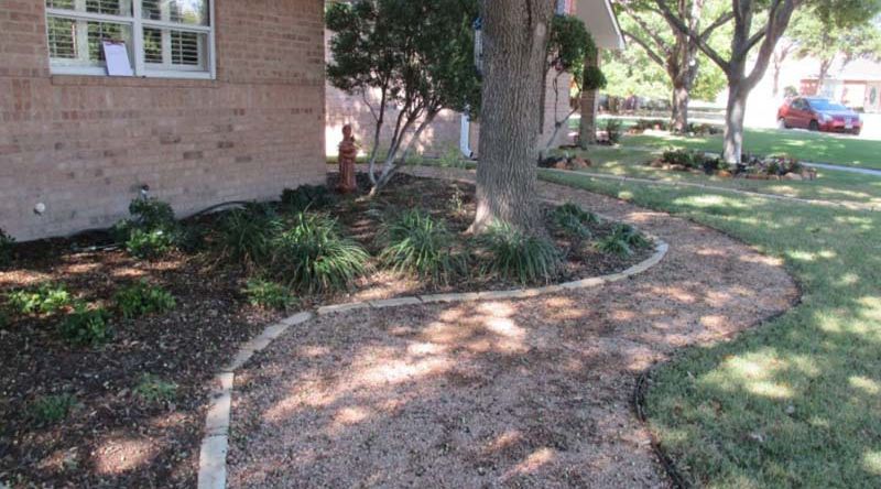 A walkway leading to a brick house with a tree in the background.