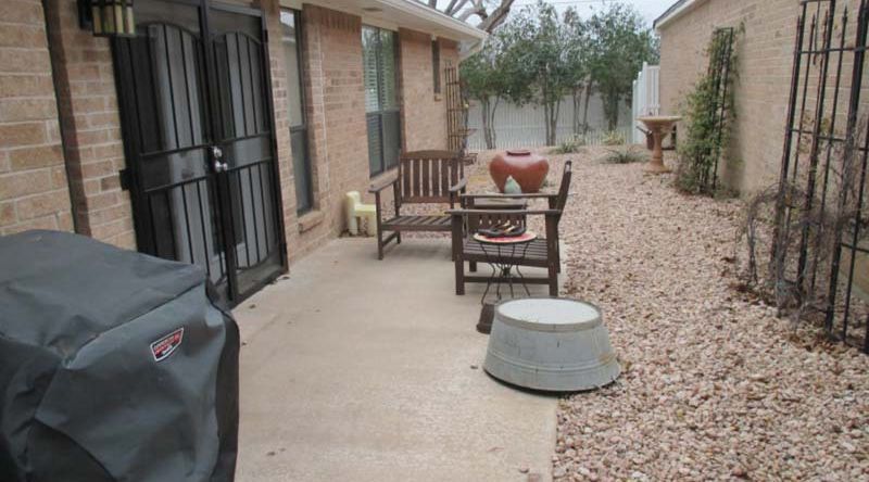 A patio with a grill and chairs in front of a brick house.