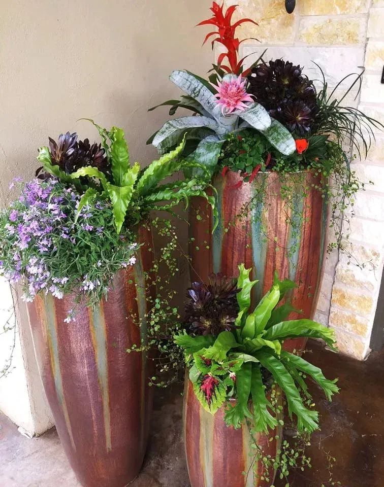 Three planters filled with flowers and ferns are sitting on a porch.