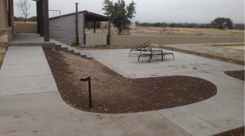 A concrete walkway leading to a patio with lawn chairs.
