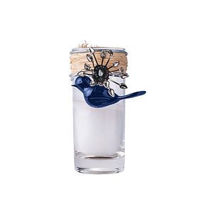 A shot glass with a blue bird on top of it.