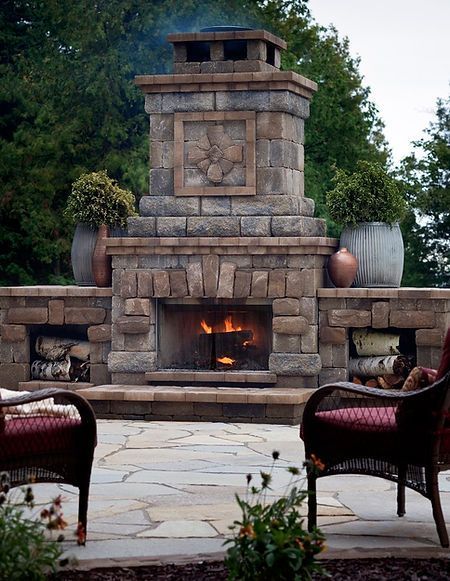 A brick fireplace is surrounded by chairs and potted plants