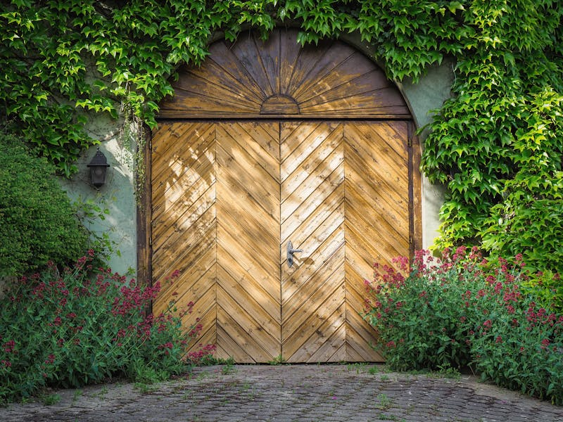 A wooden garage door is surrounded by ivy and flowers.