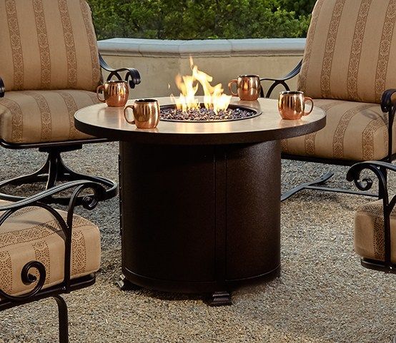 A fire pit is surrounded by chairs and copper mugs