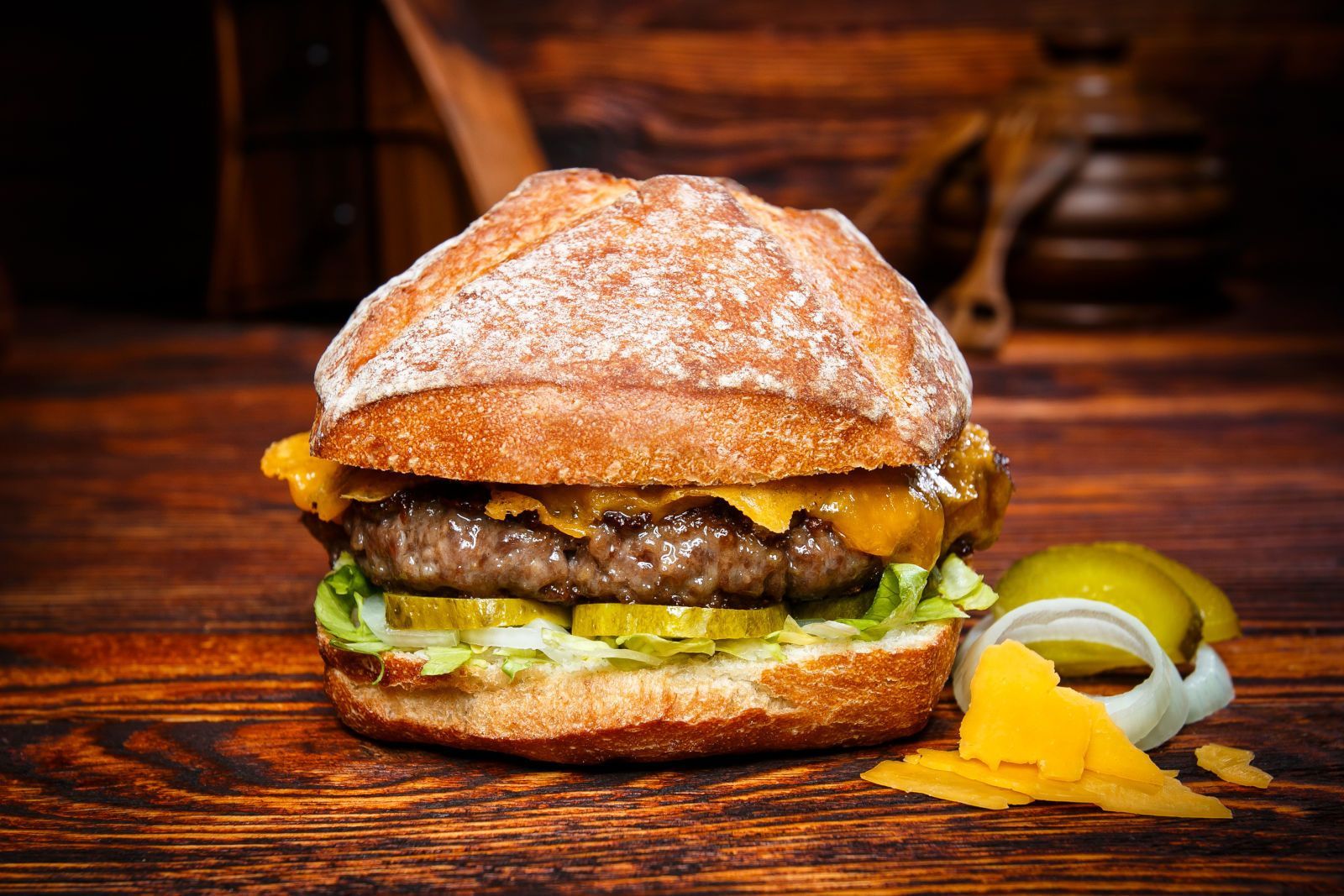 Ein Hamburger mit Käse, Salat, Gurken und Zwiebeln auf einem Holztisch.