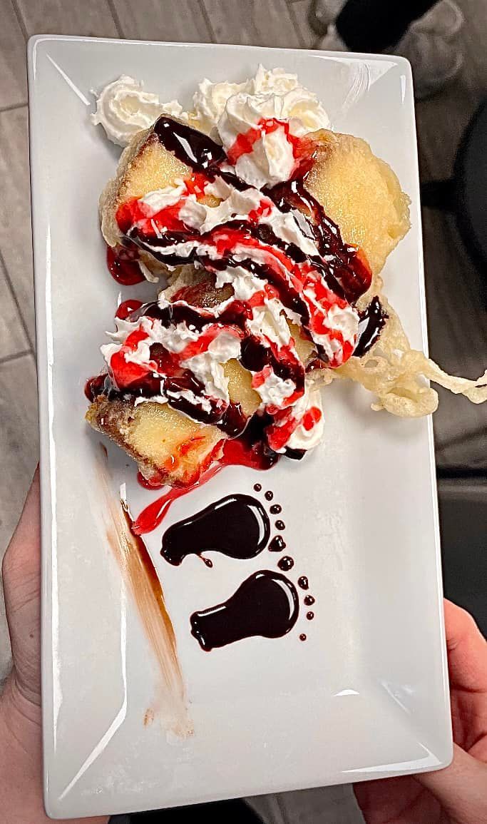 Fried dessert with whipped cream, berry and chocolate drizzle, chocolate footprints on a white plate.