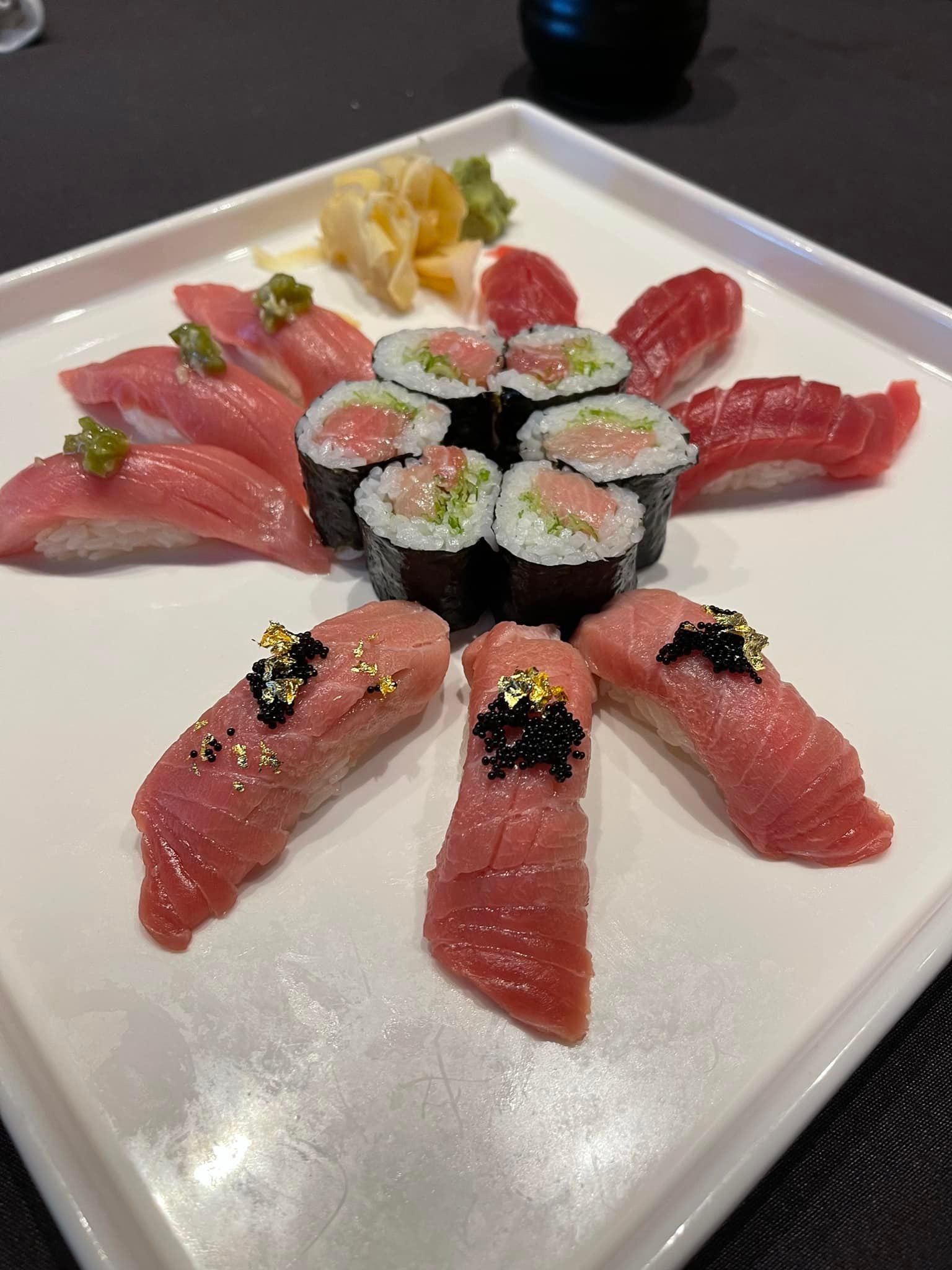 Sushi platter with tuna nigiri and rolls, arranged on a white square plate, garnished with ginger.