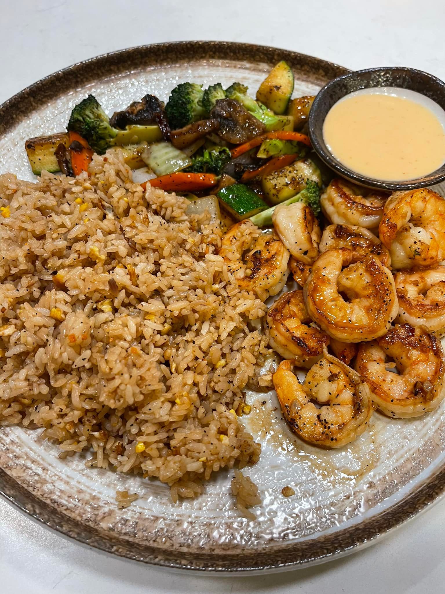 Plate of shrimp with fried rice, vegetables, and sauce.