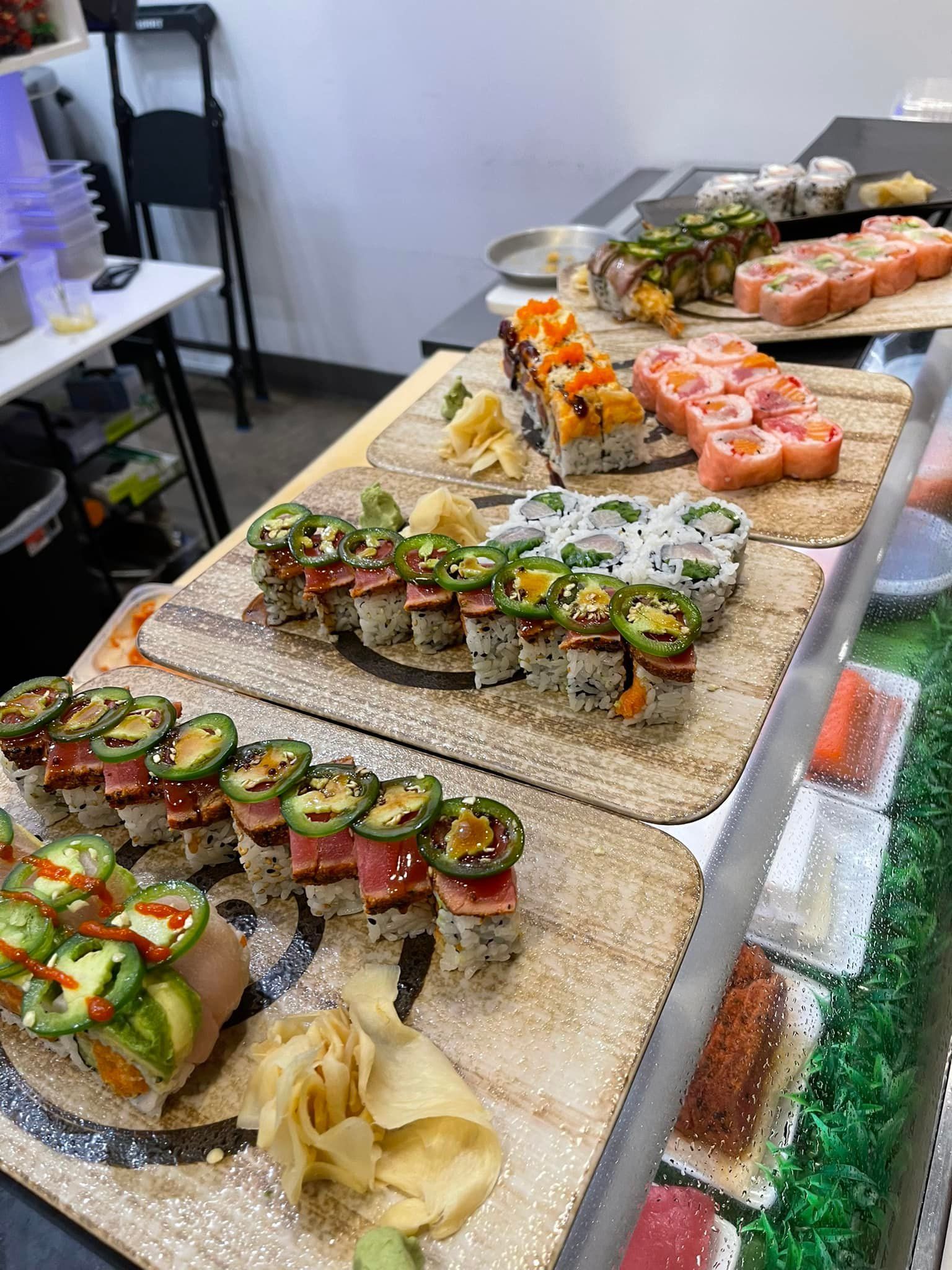 Sushi rolls on display at a restaurant, with various colorful toppings and pickled ginger.