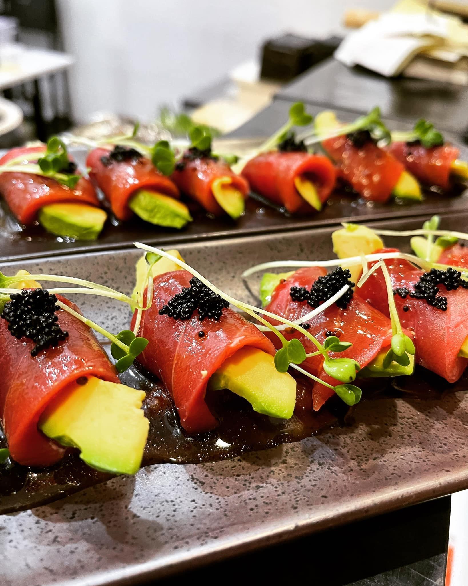 Sushi rolls with avocado, tuna, caviar, and sprouts, arranged on a dark rectangular plate.